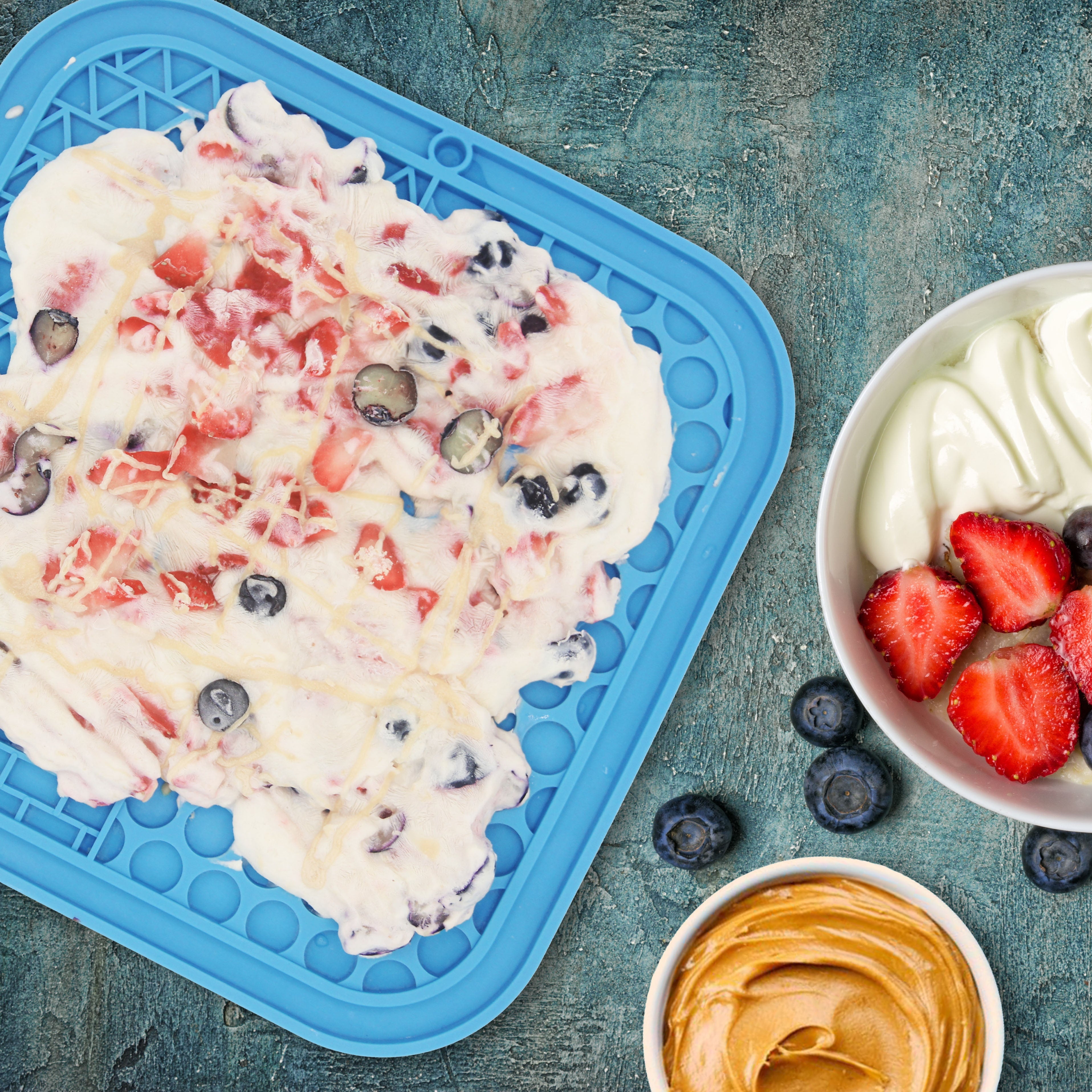 Yogurt dessert with berries on a blue tray and in a bowl on a textured blue background